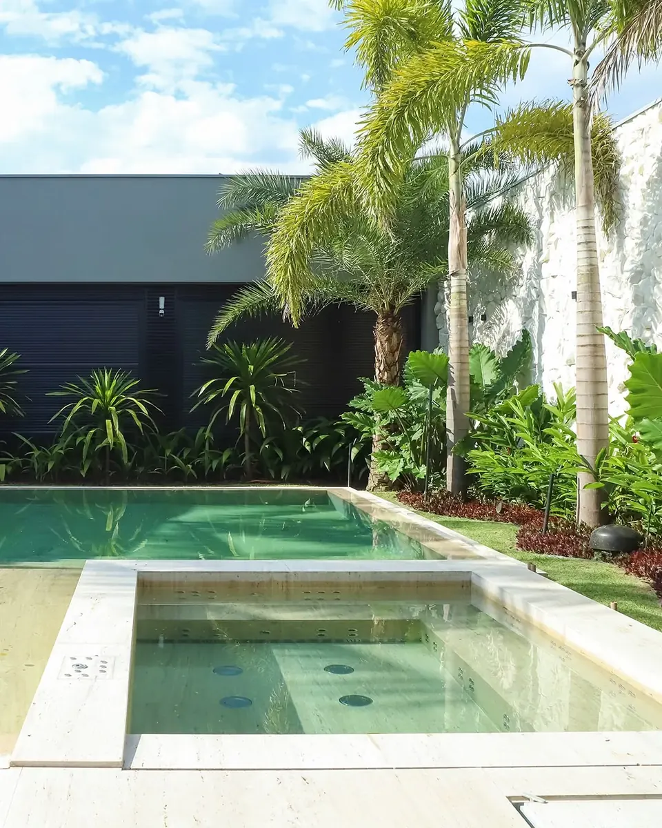 Piscina e spa com deck em pedra natural e paisagismo
